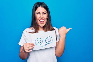 Sticker - Woman asking for psychology change holding paper with unhappy to happy emotion message pointing thumb up to the side smiling happy with open mouth