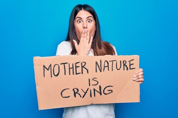 Poster - Young woman asking for environment care holding banner with mother nature is crying message covering mouth with hand, shocked and afraid for mistake. Surprised expression