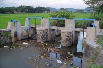 Canvas Print - River water with a pile of garbage held in irrigation dams regulating water discharge for residents' agriculture