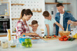 © JustLife - Mother and father making breakfast with sons. Young family preparing delicious food in kitchen.
