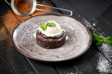 Chocolate brownie with a ball of vanilla ice cream and mint on a plate on a dark background