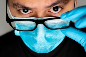 Sticker - Closeup shot of a Hispanic man wearing a blue disposable face mask and looking at the camera