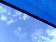 fabric sun shade and awning over patio or balcony. sun sail, spanning above city terrace. blue sky and white clouds. low angle view. metal connector and chain. summer and outdoors concept.