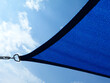 fabric sun shade and awning over patio or balcony. sun sail, spanning above city terrace. blue sky and white clouds. low angle view. metal connector and chain. summer and outdoors concept.