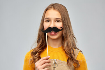 Wall Mural - party props, photo booth and people concept - teenage girl with big black moustaches showing tongue over grey background