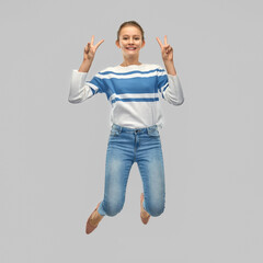 Wall Mural - people concept - smiling teenage girl in pullover jumping and showing peace hand sign over grey background