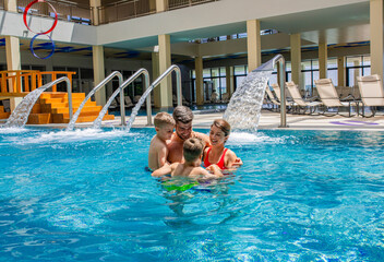 Wall Mural - smiling family of four having fun and relaxing in indoor swimming pool at hotel resort.