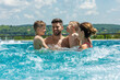 Smiling family of four having fun and relaxing in outdoor swimming pool at hotel resort.