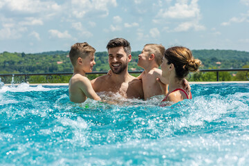 Wall Mural - smiling family of four having fun and relaxing in outdoor swimming pool at hotel resort.