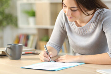 Woman reading and signing contract at home