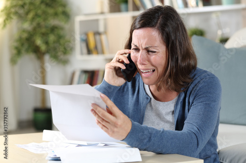 Fotografía Sad adult woman crying calling on phone with letter at home