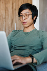 Sticker - Image of pleased asian man working with laptop while sitting