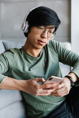 Poster - Image of concentrated asian man using cellphone and wireless headphones