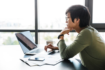 Poster - Image of serious asian man working with laptop while sitting at table