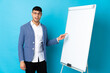 © luismolinero - Young Colombian man isolated on blue background giving a presentation on white board