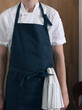 A man cook in a blue apron and a white shirt on a wooden background, a towel in his pocket