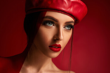 Wall Mural - Beauty fashion portrait of woman in red leather beret in studio on red background. girl with luxurious make-up. copy space