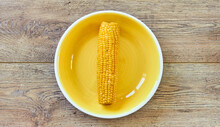 Yellow Cob Of Boiled Corn On A Yellow Plate On A Wooden Tabletop