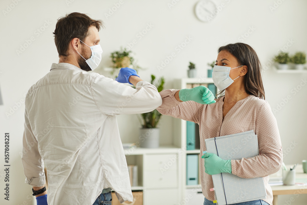 Waist up portrait of two colleagues wearing face masks bumping elbows while greeting each other at work in office - obrazy, fototapety, plakaty 