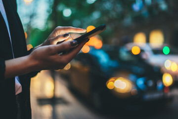 Wall Mural - Traveler woman calling mobile phone waiting yellow taxi in evening street europe city Barcelona. Girl tourist using smartphone internet online gadget cellphone on background bokeh headlights of cars