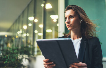 Wall Mural - side view of an elegant girl in a business black suit holding a tablet and reading correspondence,  financial adviser uses Internet technology on computer near office