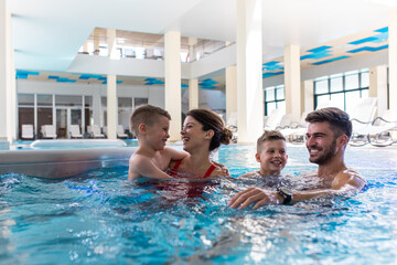 Wall Mural - smiling family of four having fun and relaxing in indoor swimming pool at hotel resort.