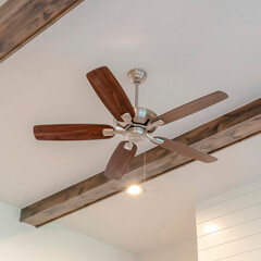 Wall Mural - Square crop Ceiling fan with lights between decorative wood beams inside living room of home