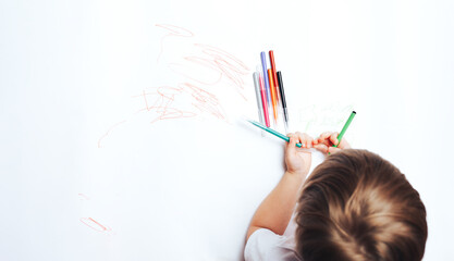 Little child draws on white paper with colored felt-tip pens, teaching children to draw