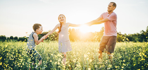 Father, son and daughter playing and having a fun in the rape fields at the sunset. People having fun on the nature. Concept of friendly family and of summer vacation.