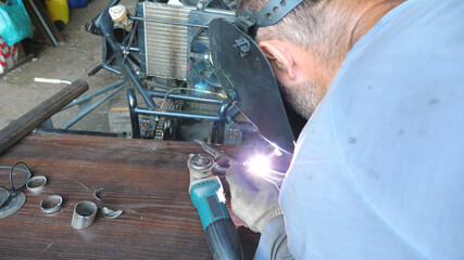 Unrecognizable welder welds metal parts in garage or workshop. Mechanic using welding machine for his work and protective mask from flashes. Slow motion Close up