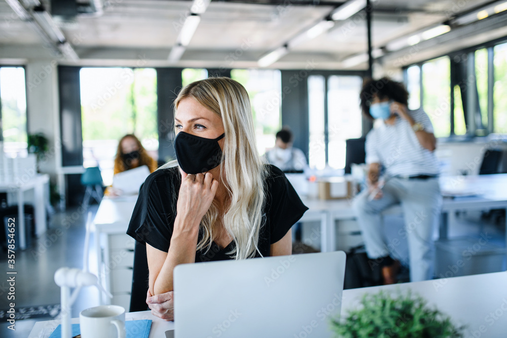 Young woman with face mask back at work in office after lockdown. - obrazy, fototapety, plakaty 