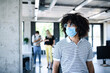 © Halfpoint - Portrait of young man with face mask back at work in office after lockdown.