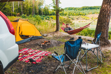 Wall Mural - man laying on hammock at lake beach near camp fire
