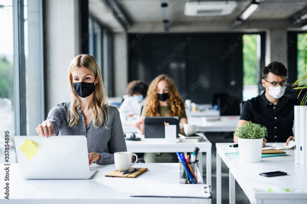 Young people with face masks back at work or school in office after lockdown. - obrazy, fototapety, plakaty 