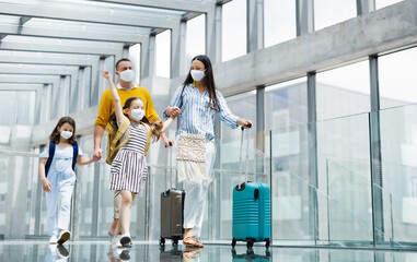 Wall Mural - Family with two children going on holiday, wearing face masks at the airport.