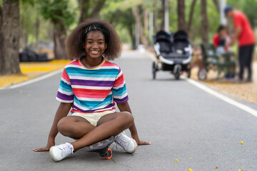 Wall Mural - Happy young girl playing on the skateboard in the park. African American girl with curly hair practicing skateboard in the garden.