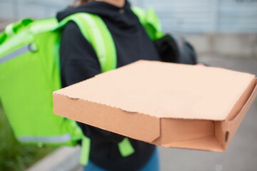 Food delivery concept. The Pizza delivery woman has a green fridge backpack. She wants to deliver faster and get to customers. She brought us food and shows how she looks.