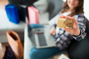 The buyer looks at the screen and holds a credit card. A young woman uses a laptop to buy a lot of goods online. She is waiting for her home delivery. close-up credit gold card.