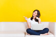© sorapop - Portrait Asian of happy beautiful young woman work from home she sitting on sofa using laptop computer in house living room pointing finger to side studio shot isolated on yellow background