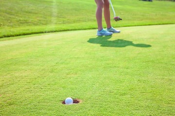 Wall Mural - Closeup of a ball into a hole at a golf course with a player in the background