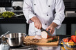 © stockbusters - Chef hands with knife slice meat at kitchen. Closeup chef hands cutting hum.