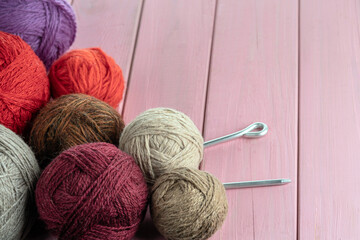 Balls of yarn in different colors with knitting needles on a background of pink wood texture. Selective focus.