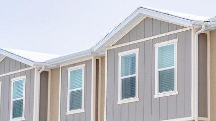 Panorama Snowy roof brick wall and vertical siding at exterior of townhome against sky