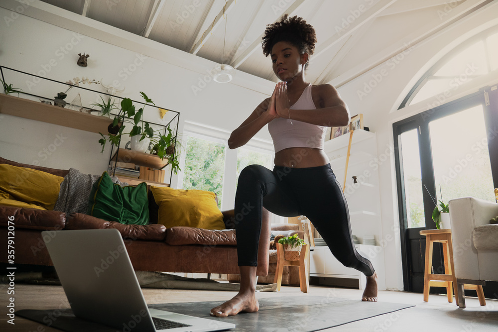 Wide angle shot of young female doing home workout or yoga from home, following an online workout on computer or online - obrazy, fototapety, plakaty 