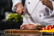 © stockbusters - Chef hands with knife and beef at kitchen. Closeup chef man hands with knife.