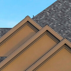 Square Home exterior with front gable roof and transom window against blue sky