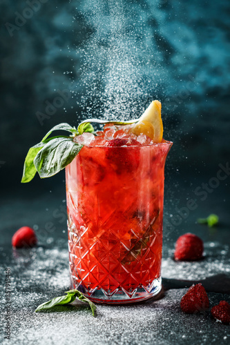 Fresh strawberry cocktail with basil, berries and powdered sugar in jar glass on dark blue background. Studio shot of drink in freeze motion, powdered sugar, drops. Summer cold drink and cocktail