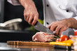 © stockbusters - Chef hands with knife cut beef at kitchen. Closeup chef man hands cut meat.