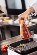 © stockbusters - Chef hand put steak on griddle pan. Closeup chef hand with fresh beef.