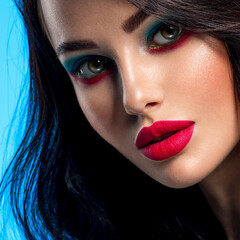 Portrait of beautiful young woman with bright blue makeup. Beautiful brunette with bright red lipstick on her lips. Pretty girl with long black hair. Closeup face of brunette woman. Sexy girl.